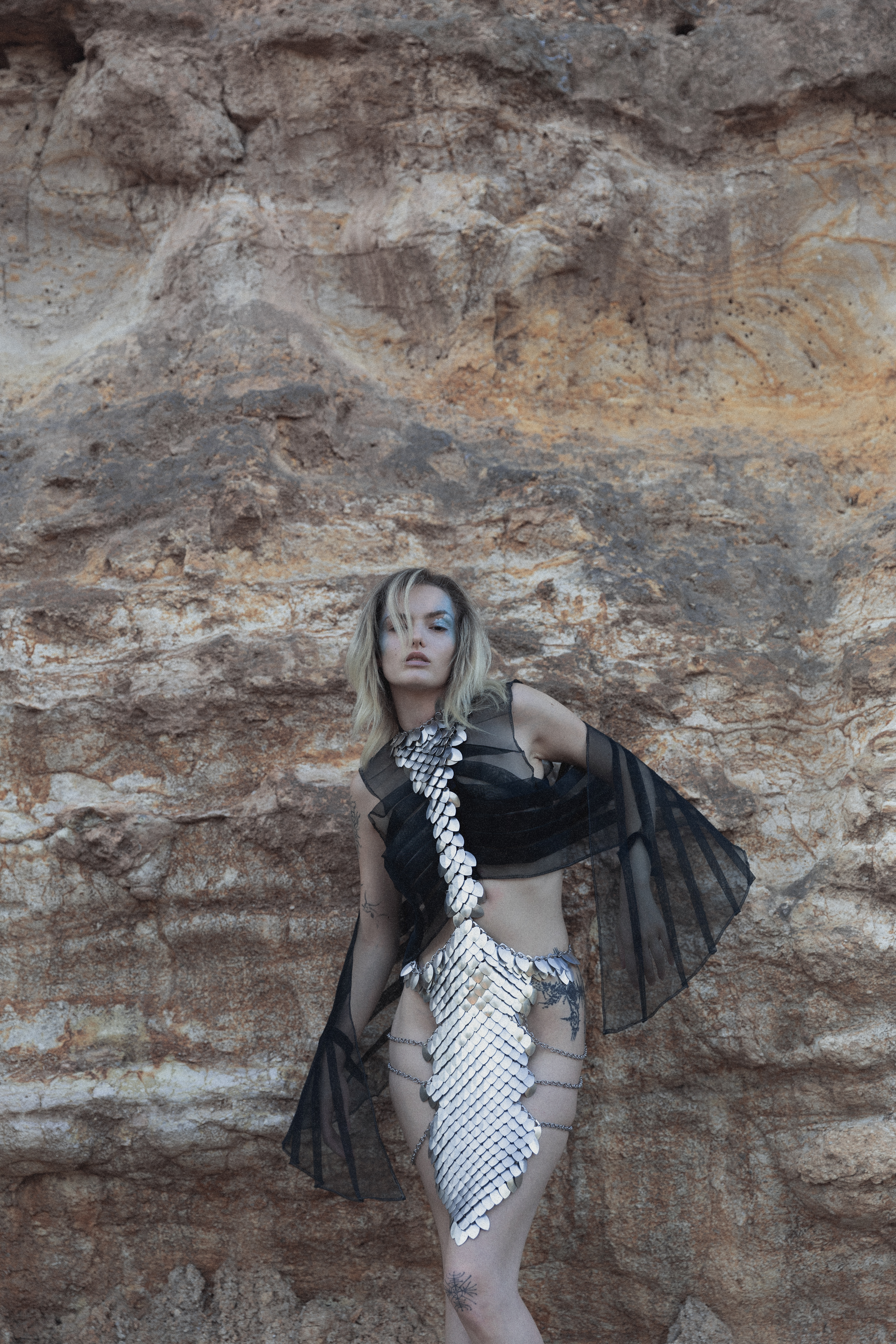 Look completo con scaglie metalliche davanti a una parete rocciosa